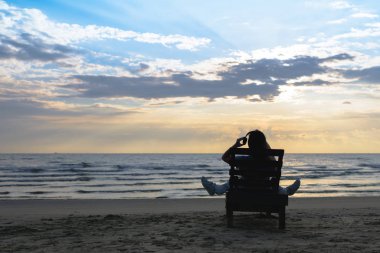 Kulaklıklı kız gün batımında plajda müzik dinleyerek şezlongda oturuyor. Yaz konsepti.