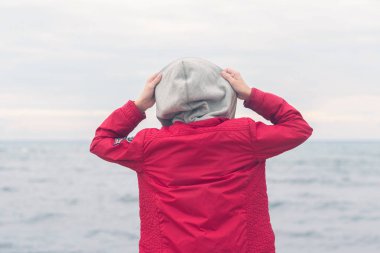 Kırmızı ceketli bir çocuk ve fırtınalı yağmurlu havalarda deniz dalgalarına bakıyor. Kavram