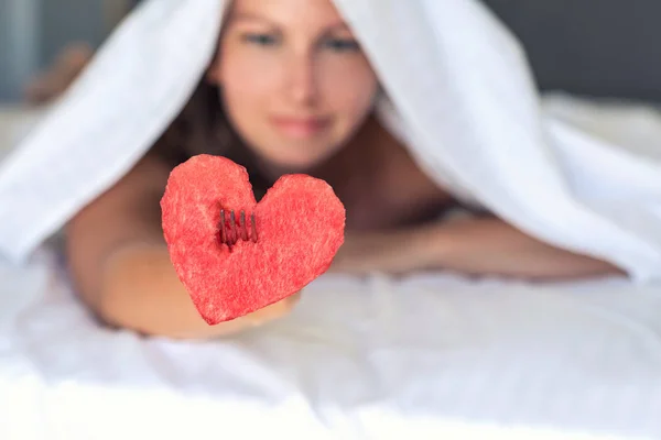 Beautiful girl in bed gives heart from watermelon on a fork. Concept