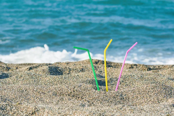 Plastic colored straws tubules for drinking in the sand on the beach. Concept