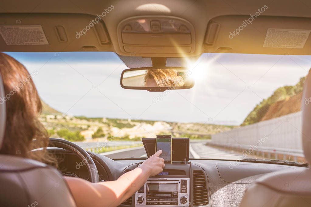 Young woman is driving on the highway in Italy and using gps navigation app on the mobile phone. View from the back seat of the car