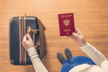 Pasaport kontrolü için havaalanında yürüyen bir bavul ve Rus pasaportu ile bir kızın üst görünümü.