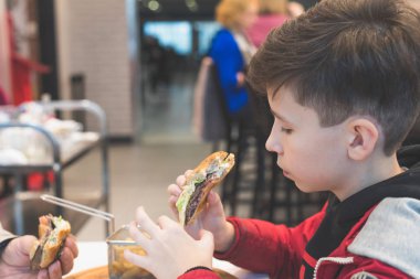 Kafede fast food yiyen çocuk. Gıda kavramı ve sağlıksız yaşam tarzı. Sepette patates kızartması ve ketçap ve soslu büyük hamburger