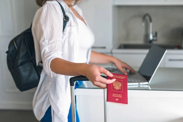 Online check in with laptop at home before travel. Female checking in to flight standing with pasport before traveling.