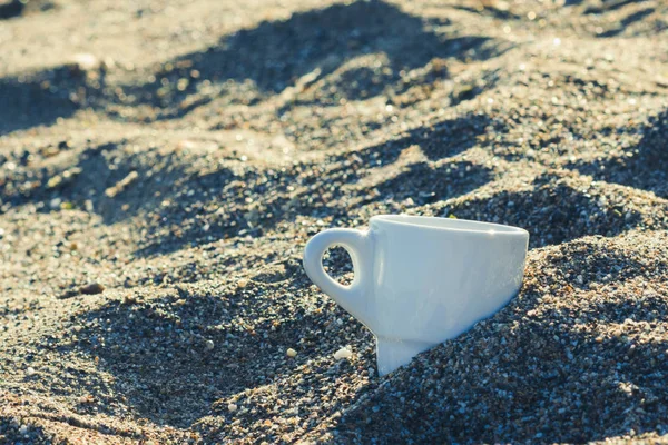 cup of coffee in the sand at sunrise on the sky background. Concept