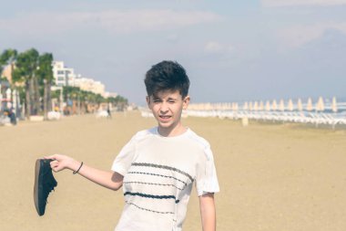 Larnaka'daki kumlu Mackenzie sahilinde spor ayakkabılı tişörtlü bir çocuk. Kıbrıs adası