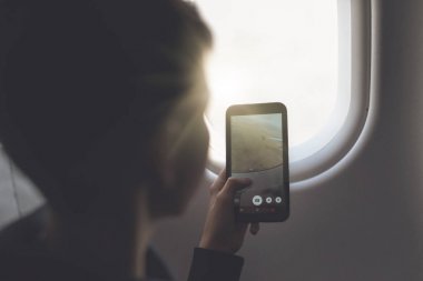 Beyaz çocuk akıllı telefon kullanıyor ve hava uçuşu sırasında fotoğraf çekiyor. Çocukla güvenlik yolculuğu. Kavram 