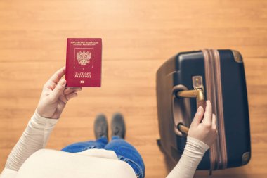 Pasaport kontrolü için havaalanında yürüyen bir bavul ve Rus pasaportu ile bir kızın üst görünümü.