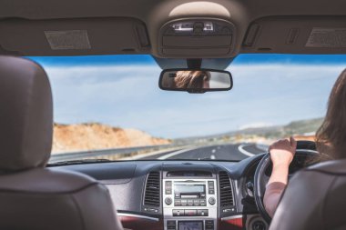 Kız Avustralya'da otobanda araba kullanıyor. Arabanın arka koltuğundan ön cam, yol ve sürücü görünümü