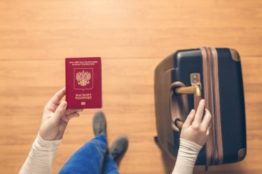 Pasaport kontrolü için havaalanında yürüyen bir bavul ve Rus pasaportu ile bir kızın üst görünümü.