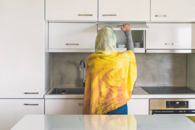 Bir eşarp müslüman bir kadın üzerinde geri görünümü bardak ve tabak ile whte dolap kapısını açar