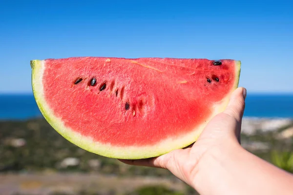 暑い夏の日に海の背景に女性の手で熟したスイカの一部 — ストック写真