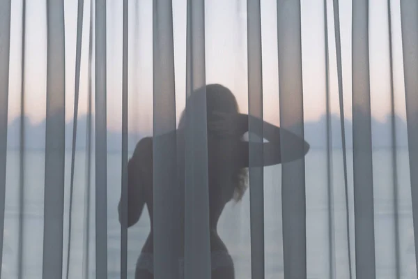 裸体美丽的女孩站在热带度假胜地日出阳台上的透明窗帘后面 — 图库照片