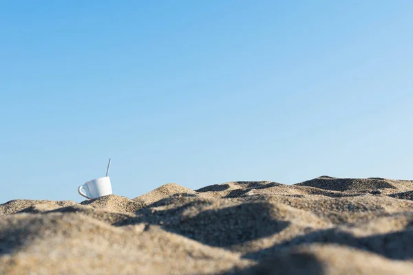 cup of coffee in the sand at sunrise near the sea. Concept