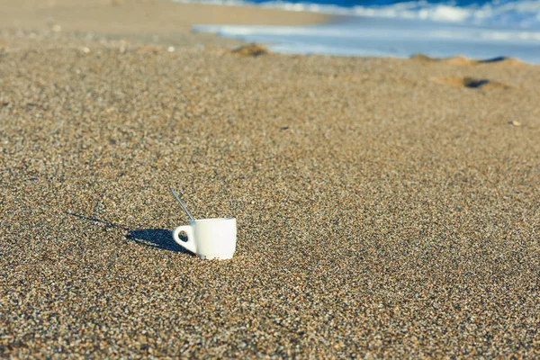 A cup of coffee in the sand at sunrise near the sea. Concept