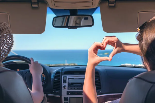 Two girls traveling by car on the Italy. One of them  holds her hands in the form of heart