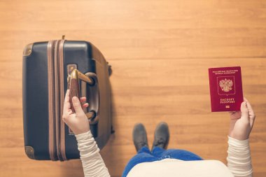 Pasaport kontrolü için havaalanında yürüyen bir bavul ve Rus pasaportu ile bir kızın üst görünümü.