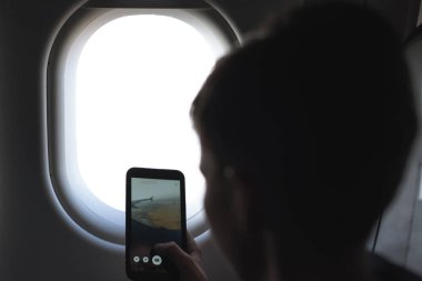 Beyaz çocuk akıllı telefon kullanıyor ve hava uçuşu sırasında fotoğraf çekiyor. Çocukla güvenlik yolculuğu. Kavram 
