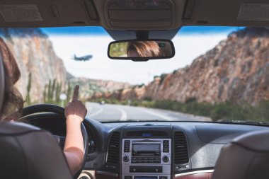 Kız Girit'te otobanda araba kullanıyor. Arabanın arka koltuğundan ön cam, yol ve sürücü görünümü