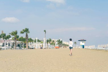 Larnaka'daki kumlu Mackenzie sahilinde spor ayakkabılı tişörtlü bir çocuk. Kıbrıs adası