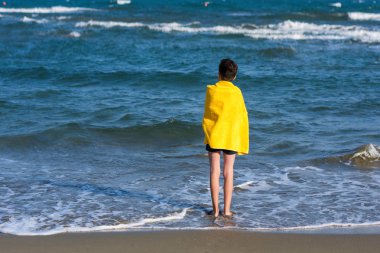 Sahil üzerinde sarı Havlu ayakta çocuğun arka görünümü babasının denizde dalış bekliyor. Aile konsepti.
