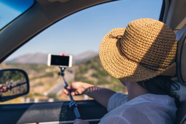 Blogger kız hasır şapka lı akıllı telefon ve selfie çubuğu kullanarak selfie fotoğrafı veya video çekiyor. Tatil ve turizm konsepti