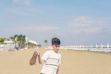 Larnaka'daki kumlu Mackenzie sahilinde spor ayakkabılı tişörtlü bir çocuk. Kıbrıs adası