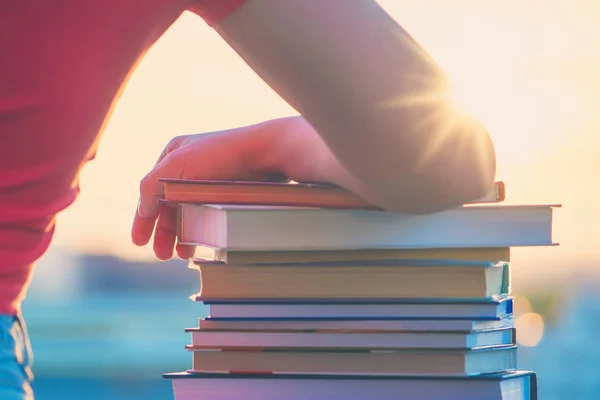 Female student with a lot of books preparing for university exam late evening on the sunset town background. Education concept