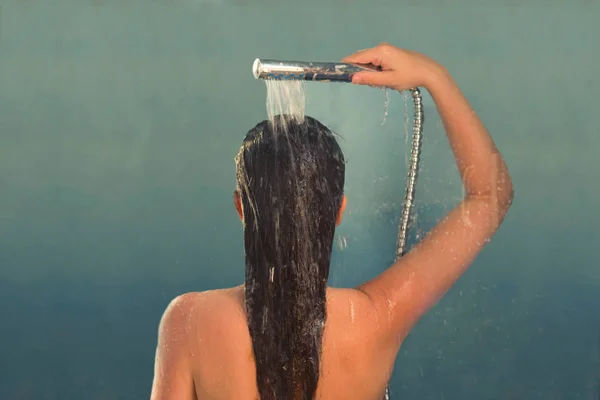 シャワーキャビンでシャワーを浴びる美しい裸の若い女性のバックビュー 透明なガラスドアの落下 — ストック写真