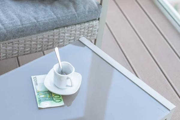 One hundred euro and empty cup of coffee on a glass table of outdoor cafe. Payment, tip.