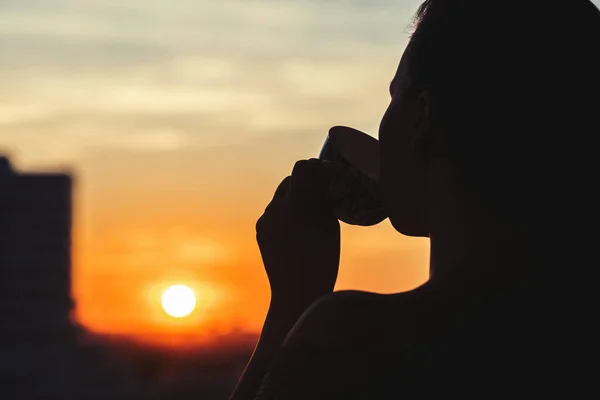 女孩在日落时分喝杯茶的剪影 从上面看城镇 — 图库照片