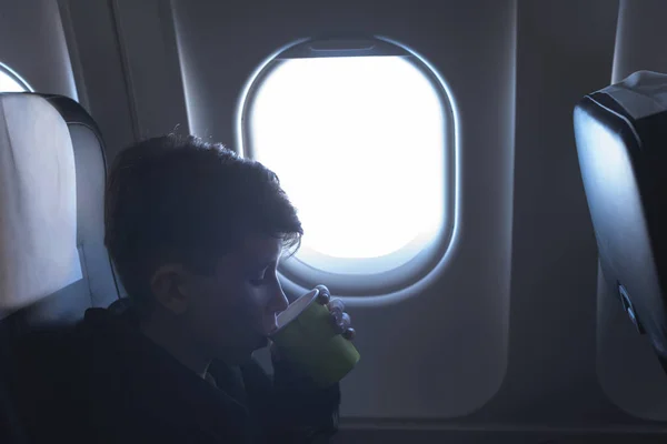 飛行機の窓の近くに座っている紙コップから飲んでいる少年 機内食 — ストック写真