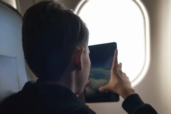 白人の少年はシートベルトを締め タブレットPcを使用して 空中飛行中に写真を撮ります 子供との安全旅行 — ストック写真