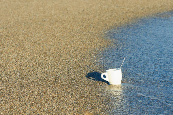 A cup of coffee in the sand at sunrise near the sea. Concept