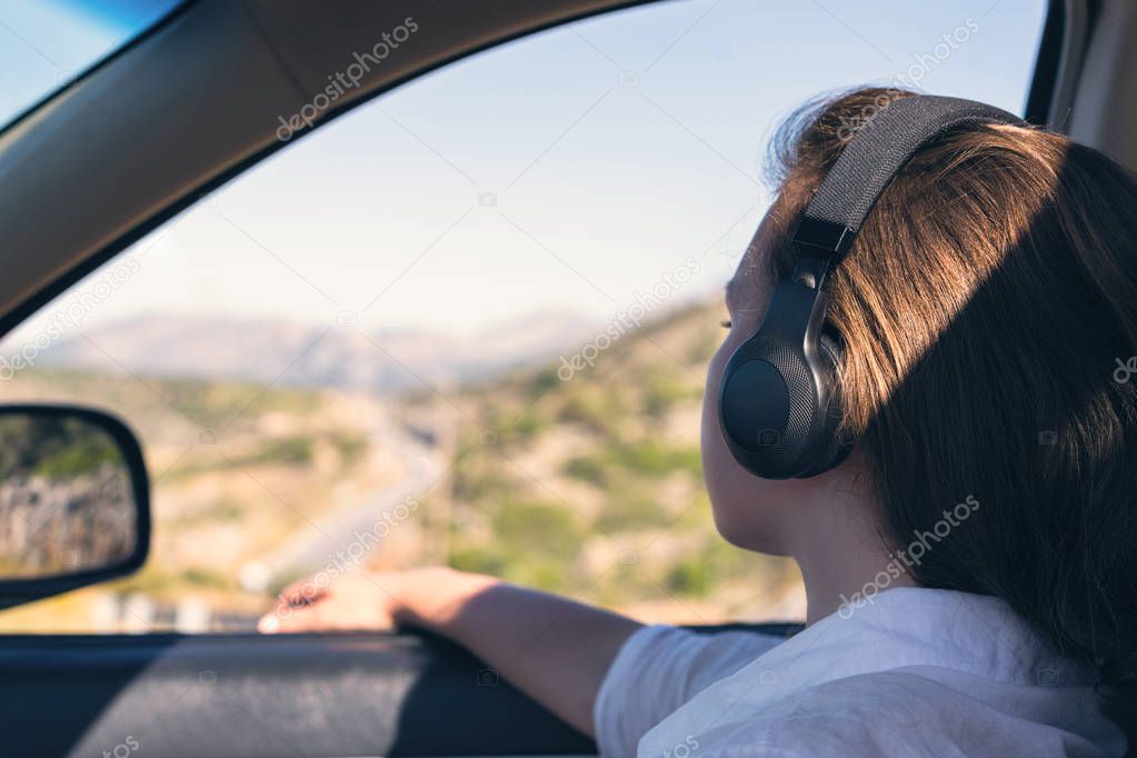 Blogger girl in the headphones taking selfie picture or video using smartphone and selfie stick inside of car