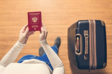 Pasaport kontrolü için havaalanında yürüyen bir bavul ve Rus pasaportu ile bir kızın üst görünümü.