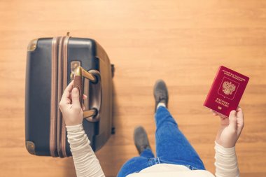 Pasaport kontrolü için havaalanında yürüyen bir bavul ve Rus pasaportu ile bir kızın üst görünümü.