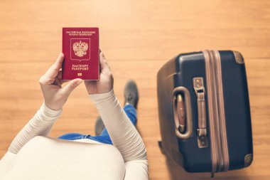 Pasaport kontrolü için havaalanında yürüyen bir bavul ve Rus pasaportu ile bir kızın üst görünümü.