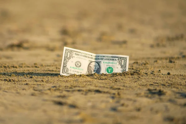Banknote of value of one dollar in the the sand on the beach. Concept of cheap travel and vacation. Promotion and discount