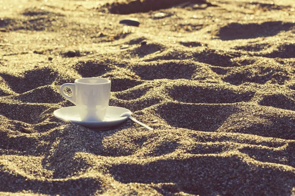 cup of coffee in the sand at sunrise on the sky background. Concept