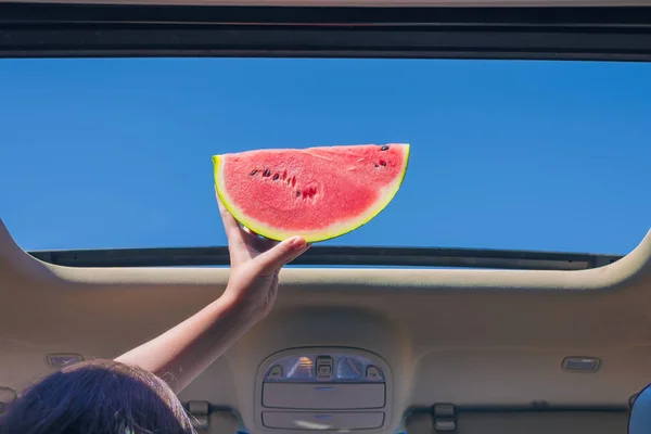 Two girls traveling by car and holding slice of watermelon in open hatch of a vehicle. Travel concept