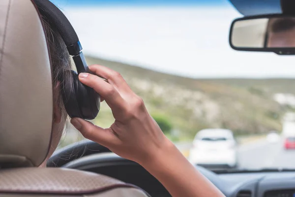 The girl in the headphones is driving on the highway in Italy. View from the back seat of the car on the windshield, road and the driver