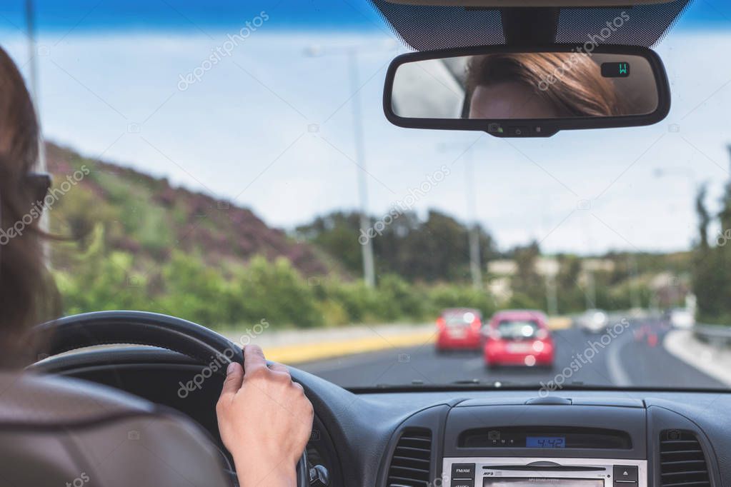 The girl is driving on the highway in Spain. View from the back seat of the car on the windshield, road and the driver