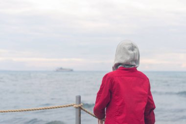 Kırmızı ceketli bir çocuk ve fırtınalı yağmurlu havalarda deniz dalgalarına bakıyor. Kavram