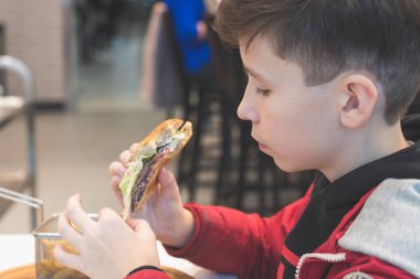 Kafede fast food yiyen çocuk. Gıda kavramı ve sağlıksız yaşam tarzı. Sepette patates kızartması ve ketçap ve soslu büyük hamburger