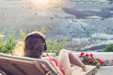 Kulaklık ve mayo kız gün batımında bahçesinde şezlong üzerinde yatıyor.