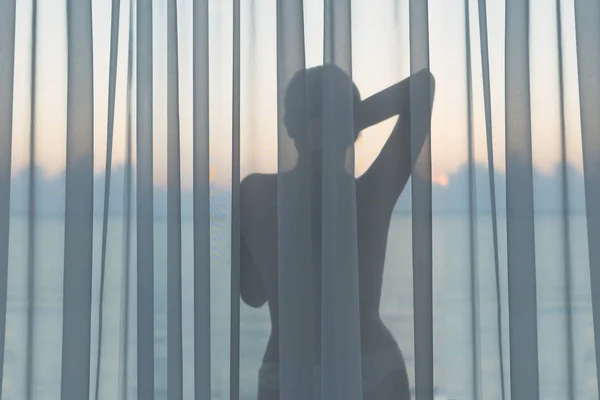 赤裸裸的美丽女性穿着蕾丝内裤站在日出清晨玻璃阳台透明窗帘后面 — 图库照片