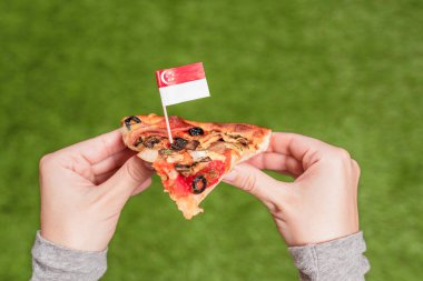 Bir kürdan şeklinde Singapur bayrağı ile kadın elinde pizza bir dilim. Yeşil çimenlerin üzerinde öğle yemeği. Çin. Kavram