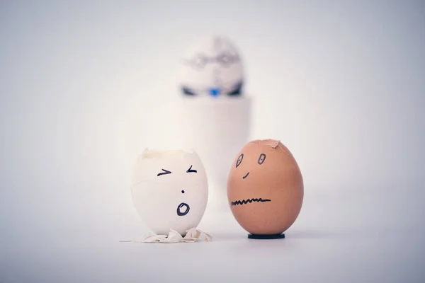Two broken eggs employee in the form of human head (white and black) complain to each other. Boss egg on the background.