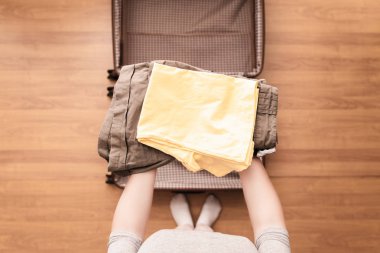 Yeni bir yolculuk için bir bagaj (bavul) bir yürüyüş için giysi ambalaj kadın elleri üst görünümü. 